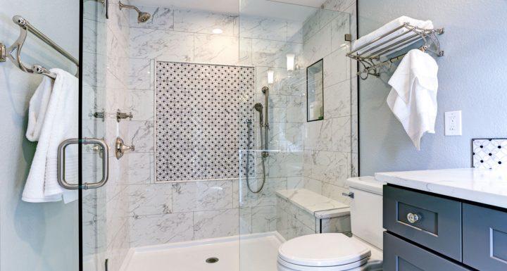 Elegant bathroom featuring a glass-enclosed shower with white marble tiles and a striking mosaic accent wall. The room includes chrome fixtures, a classic white toilet, and a vanity with a dark grey cabinet and marble countertop. Additional touches like a towel rack and soft lighting enhance the sophisticated and clean design.